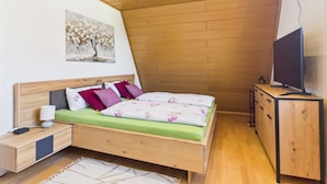 Une chambre avec un plafond en bois, un lit avec une literie verte, une table de chevet, un téléviseur posé sur un meuble en bois et un tableau accroché au mur.