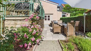 Une terrasse dotée de meubles en osier, d’un mur en pierre et de fleurs roses.