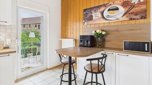 Une cuisine avec un plafond en bois, une machine à café, un vase rempli de fleurs et une vue sur l’extérieur, visible à travers une porte vitrée.
