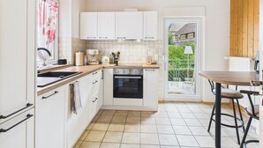 Une cuisine compacte avec des meubles blancs, une cuisinière et un petit coin repas équipé de tabourets.