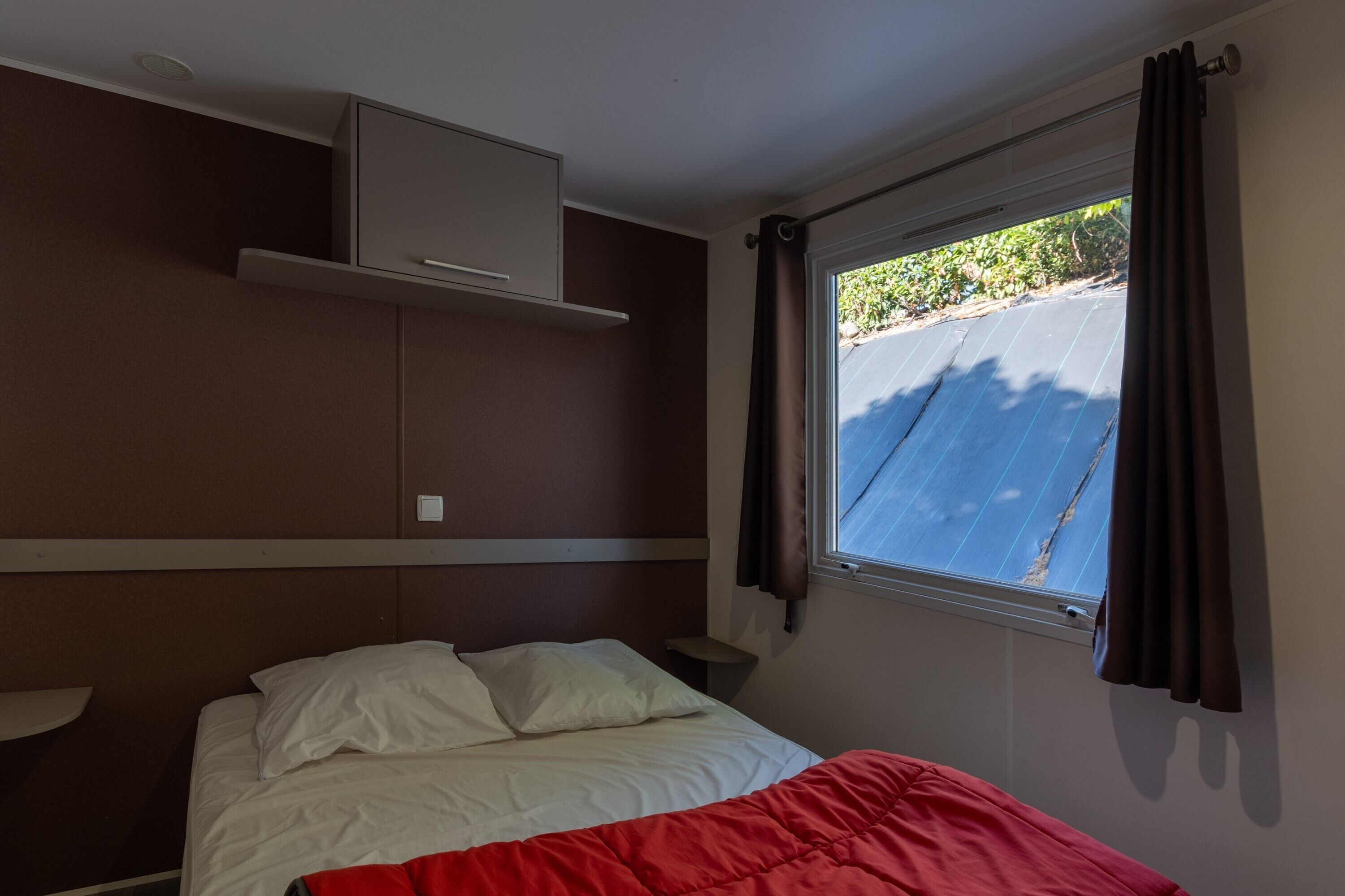 A room with a bed, a window with curtains, a wall-mounted air conditioning unit, and a small table.