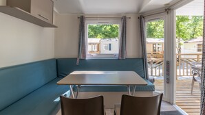 A room with a blue sofa, a table, and chairs. - Mobile Home 'Mobil-home Confort B - 1-8 Pers' with Shared Pool and Shared Garden (Lavilledieu)