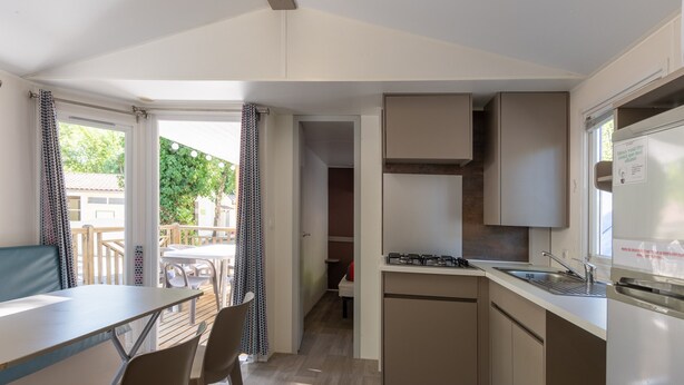 A compact kitchen with a gas stove, sink, and a dining area with chairs and a table. - Mobile Home 'Mobil-home Confort B - 1-8 Pers' with Shared Pool and Shared Garden (Lavilledieu)