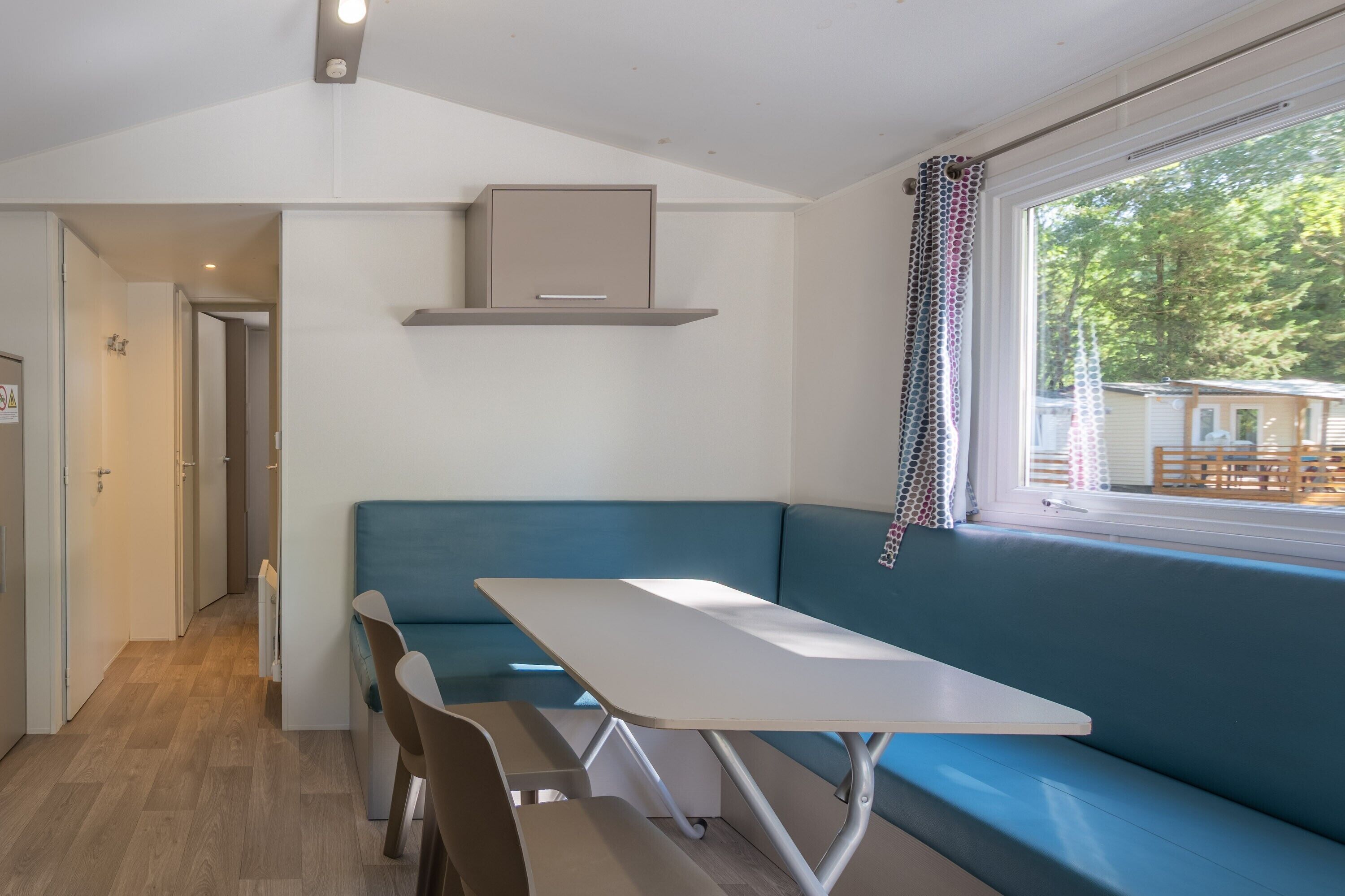 Ein Zimmer mit einer blauen Bank, einem weißen Tisch und einem Fenster mit Vorhängen.