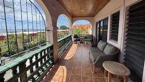 A covered balcony with a view of the sea, a seating area with a table, and a small stool.