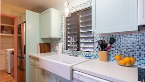 A kitchen with light blue cabinets, a white countertop, a window with a metal rack, and a bowl of lemons on the counter.