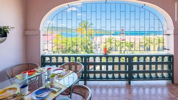 A balcony with a view of the sea, a table set with plates and cups, and a chair.