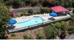 An aerial view of a pool area with a red-roofed building, lounge chairs, and umbrellas.