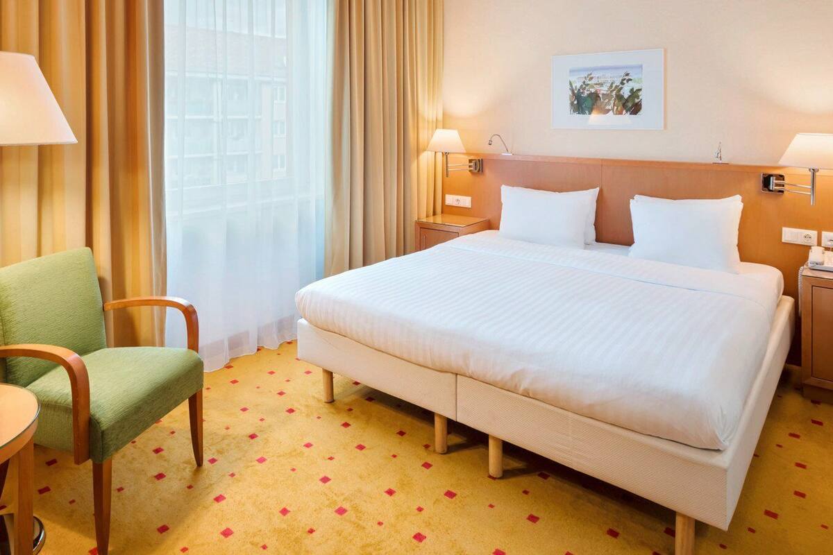A hotel room with a large bed, two bedside lamps, a chair, a small table, and a picture on the wall.