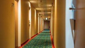 Een lange, smalle hotelgang met een patroon in het tapijt en deuren aan beide zijden.