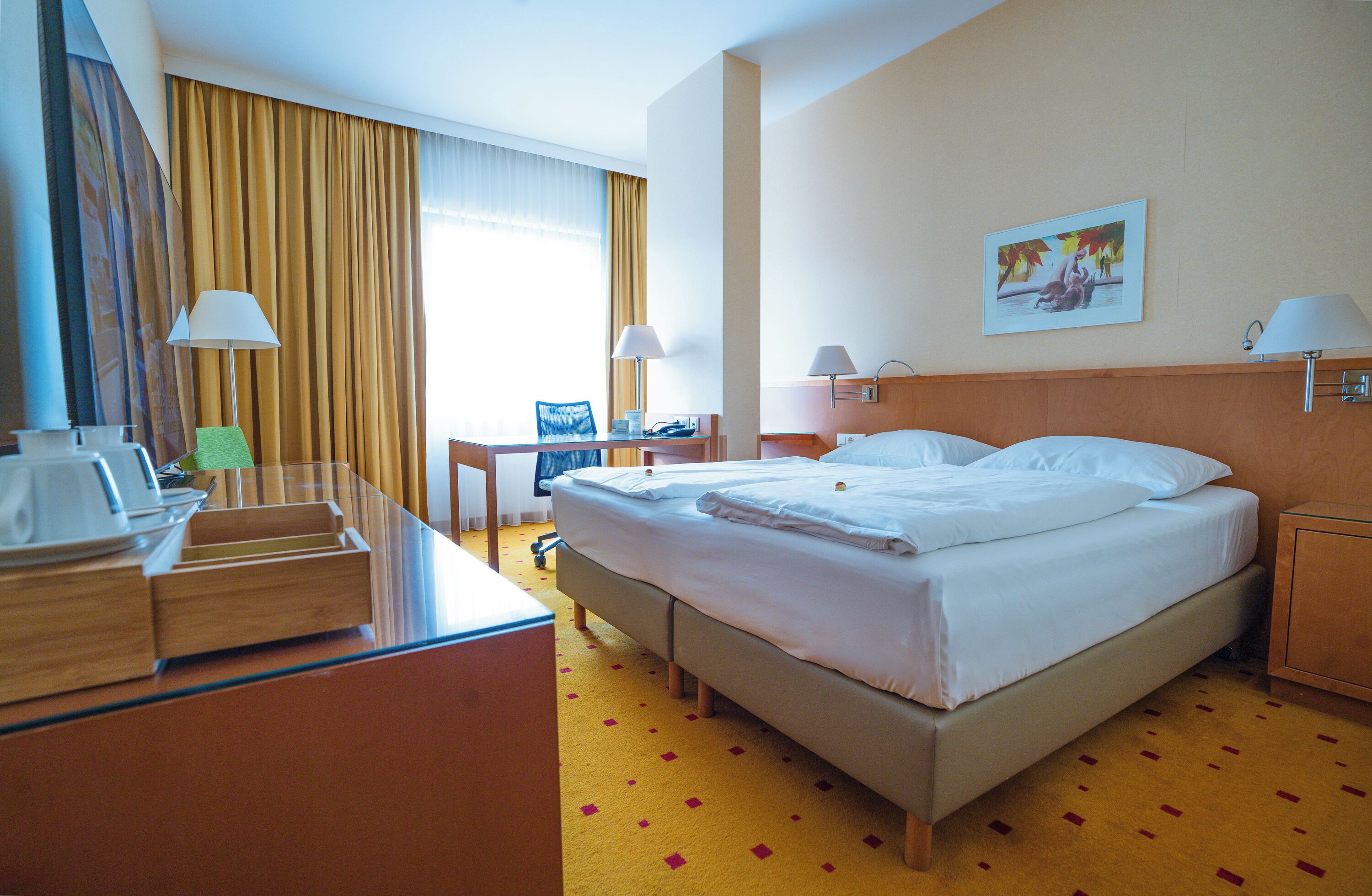 Een hotelkamer met een bed, bureau, stoel, lampen en een schilderij aan de muur.