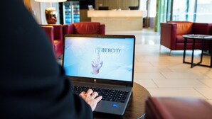 Iemand gebruikt een laptop in een moderne hotellobby met rode zitplaatsen en een receptie op de achtergrond.