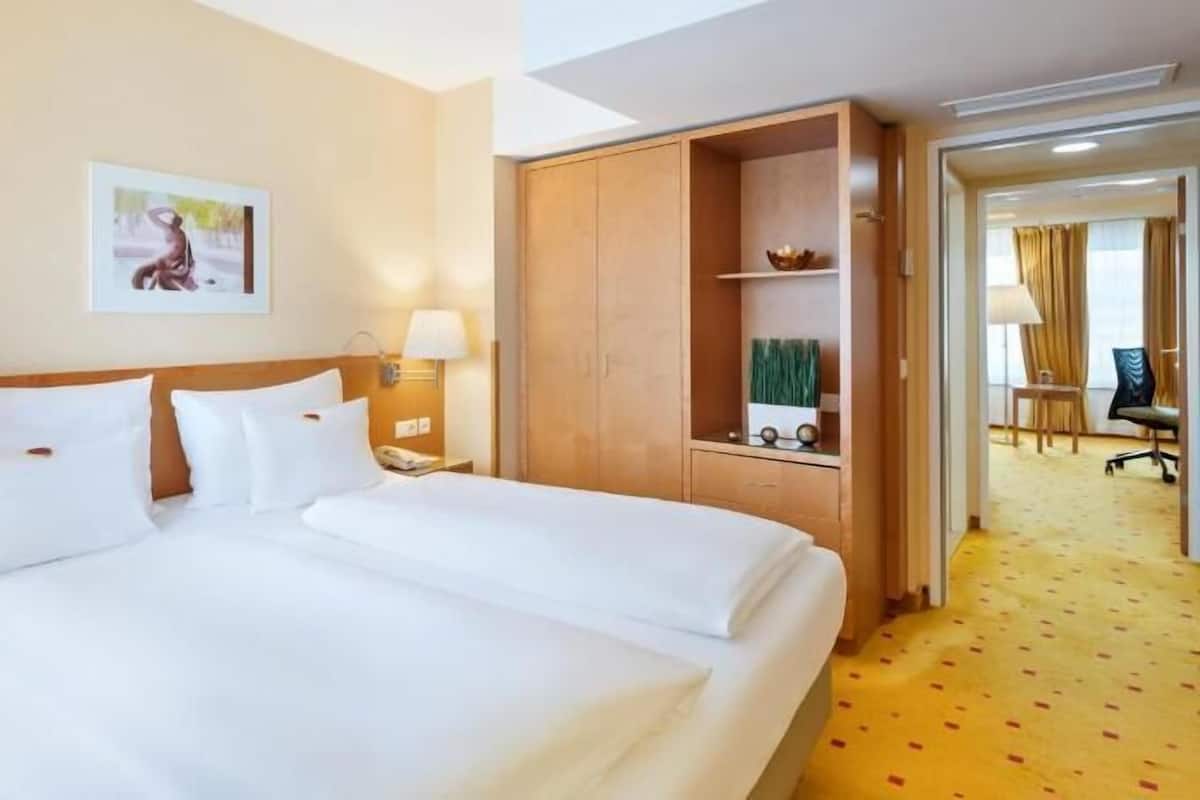 A hotel room with a large bed, two bedside tables, a desk, a chair, and a small bathroom area.