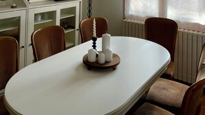 A dining area with a round table, chairs, a ship model, a lamp, and a window with curtains.