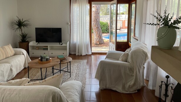A living room with a television, sofa, and a view of a swimming pool.