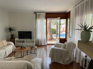 A living room with a television, sofa, and a view of a swimming pool.
