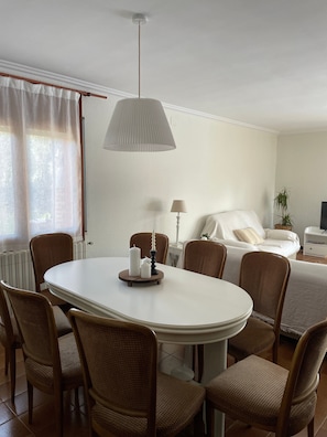 A dining area with a round table, wicker chairs, a white lamp, and a bed with a white duvet in the background. - Holiday Home 'Rocaclara' with Private Pool, Garden, and Wi-Fi (Mont-ras)