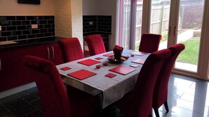 A dining area with a table set for four, red chairs, and a view of the backyard through a sliding glass door. - Sheffield Hillside Retreat (Sheffield)