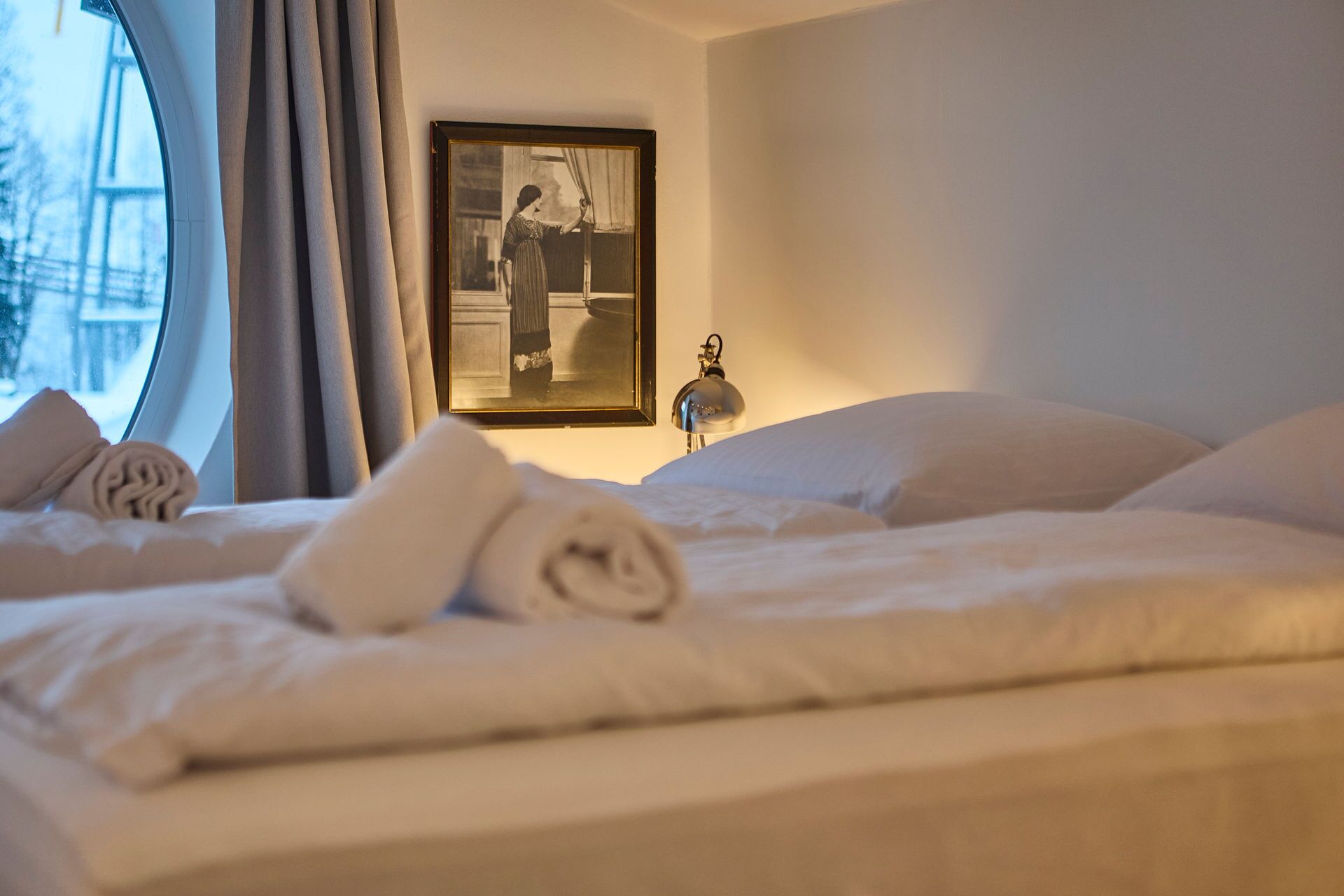 Een hotelkamer met een bed, een ingelijst beeld aan de muur en een raam met gordijnen.