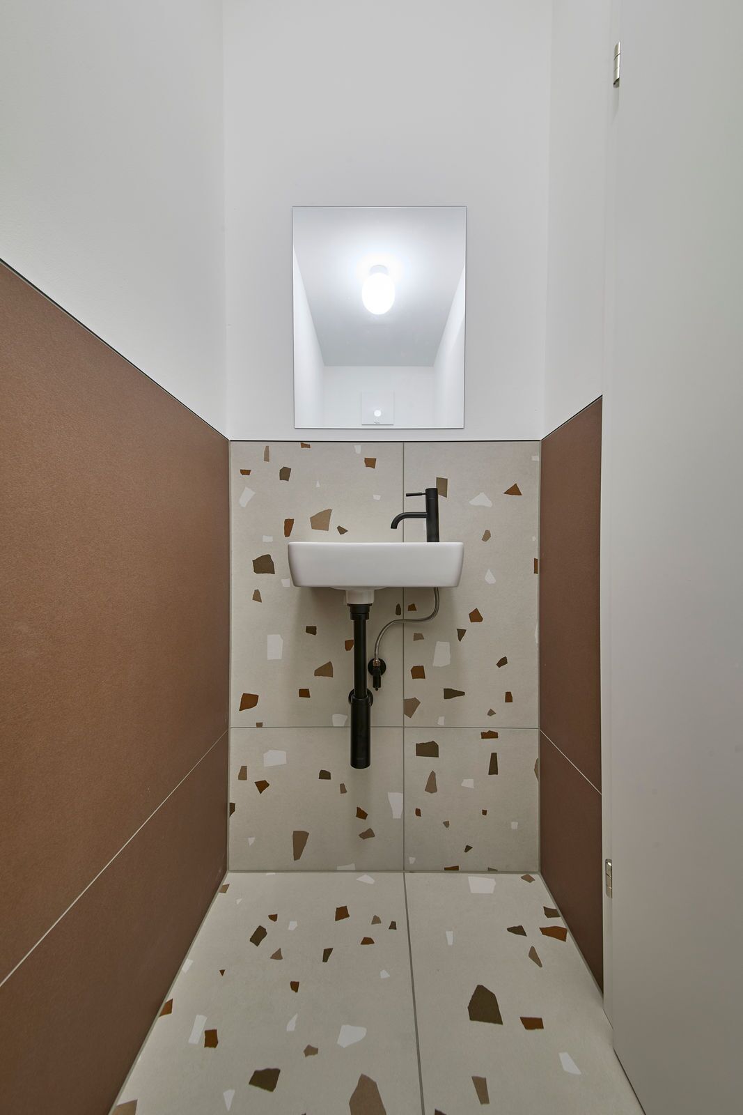 Un bagno piccolo con un lavandino bianco, uno specchio sopra e una parete decorata con un motivo terrazzo.