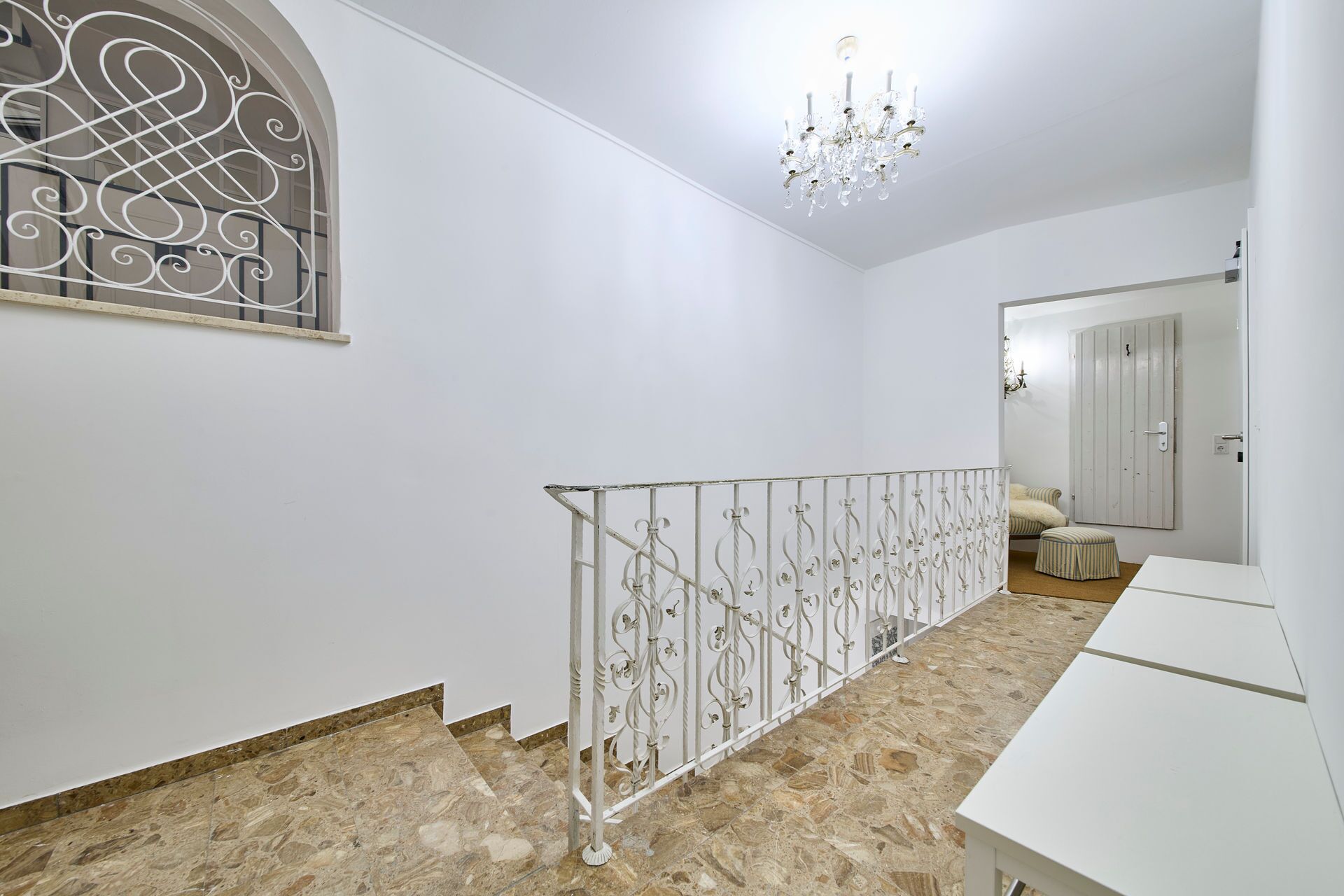 A hallway with a decorative metal railing, a chandelier, and a door leading to another room.