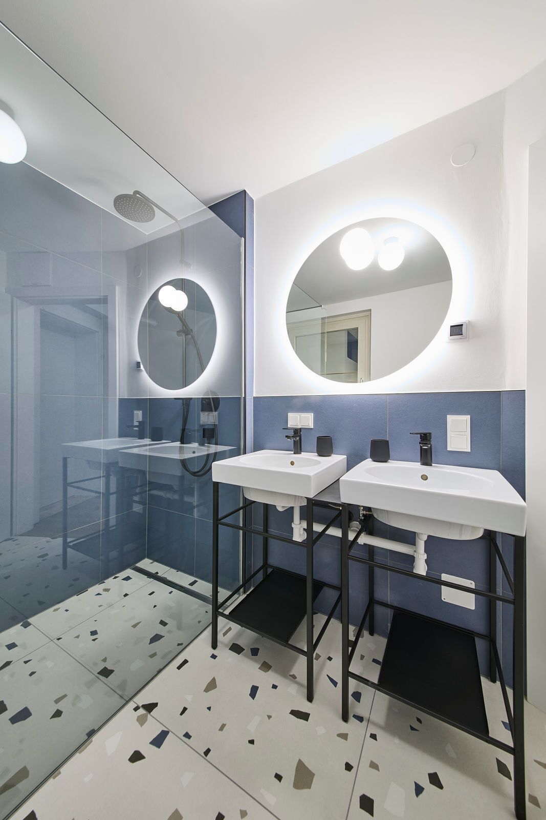 Een moderne badkamer met twee wastafels, een douche en een grote spiegel met ingebouwde verlichting.