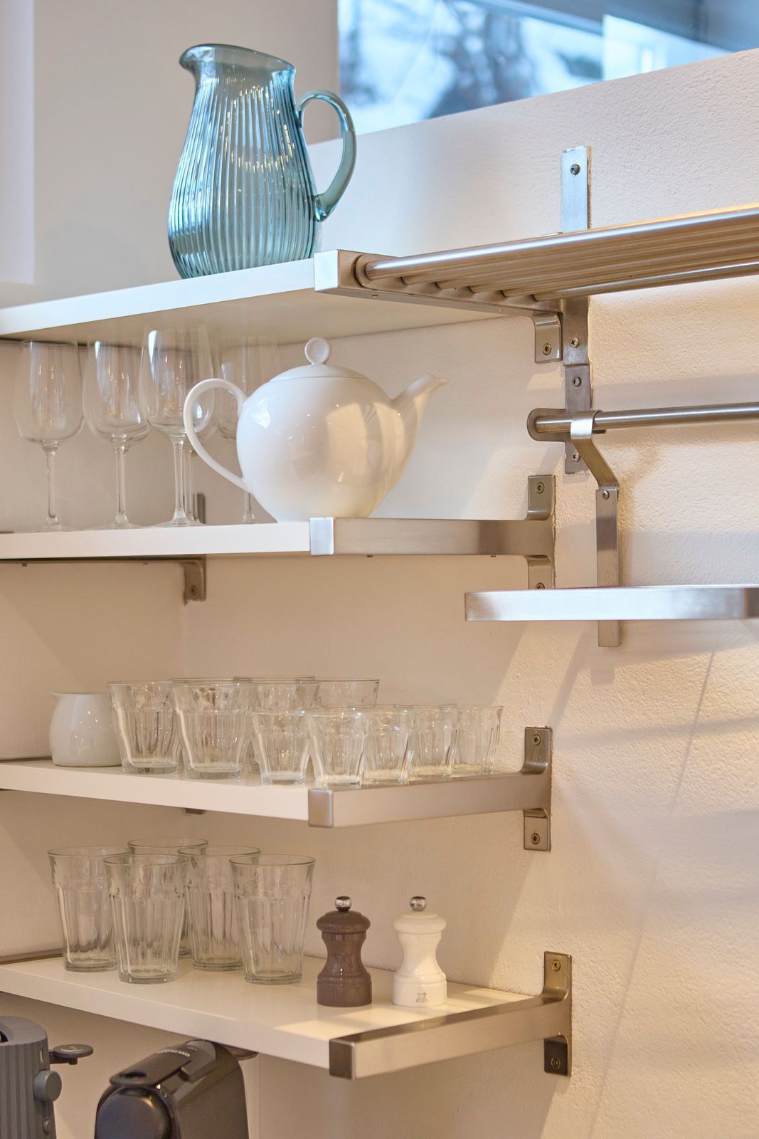 Une cuisine avec des étagères blanches où sont rangés différents objets en verre et une bouilloire.