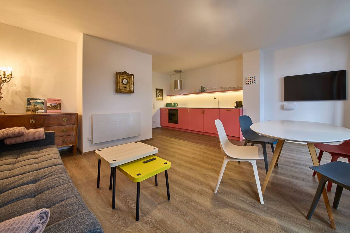 A modern living room with a sofa, a small table, and a dining area with chairs.