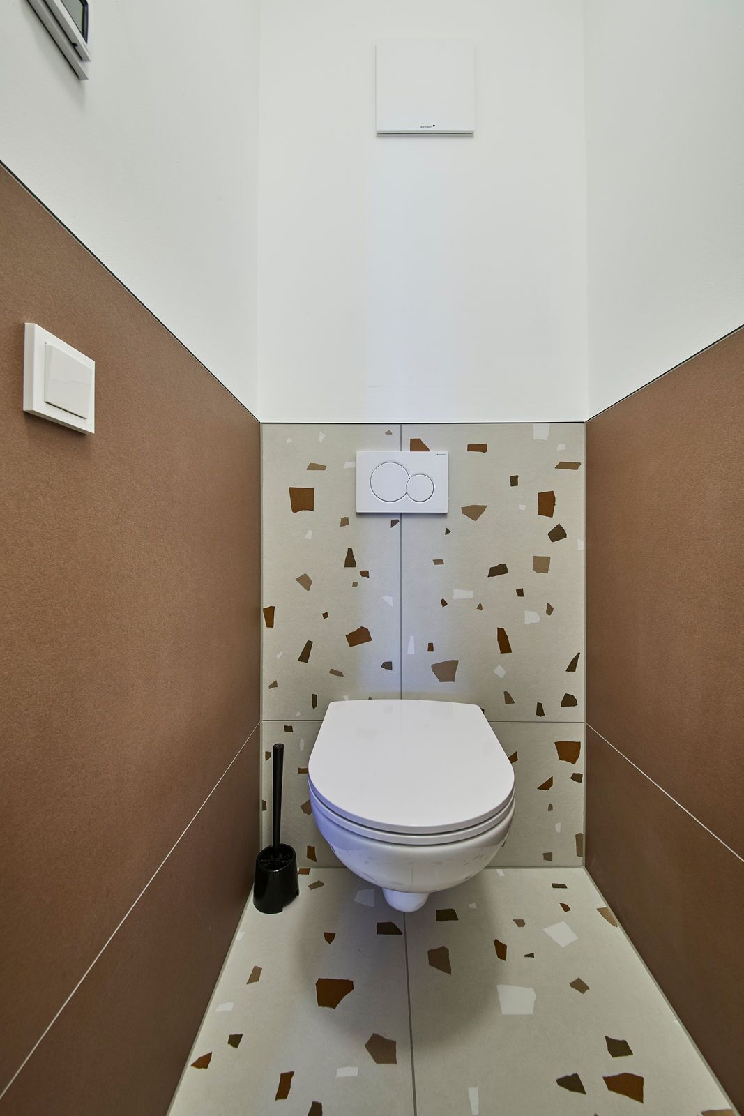 A small, modern bathroom with a toilet, a hand dryer, and a wall-mounted light switch.