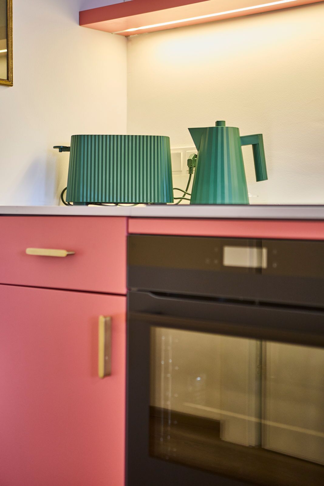 A kitchen with a pink cabinet, a green kettle, and a black oven.