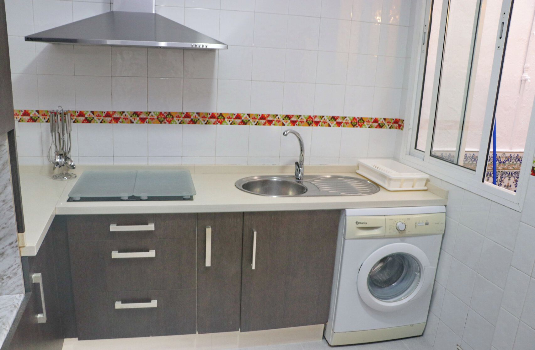 Une petite cuisine équipée d’un évier, d’un lave-linge et d’une fenêtre.