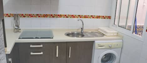 Cocina compacta con lavamanos, lavadora y ventana.