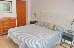 Un dormitorio con cama, cómoda, mesita de noche, lámpara y un cuadro en la pared.