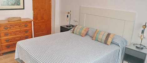 Une chambre à coucher avec un lit, une commode, une table de chevet, une lampe et un tableau encadré au mur.