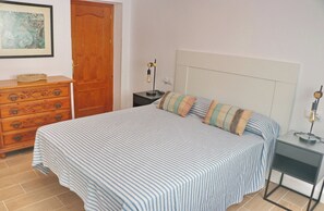 Une chambre à coucher avec un lit, une commode, une table de chevet, une lampe et un tableau encadré au mur.