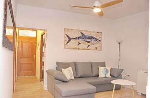 A living room with a grey sofa, a small white table, a ceiling fan, and a wall-mounted fish painting.