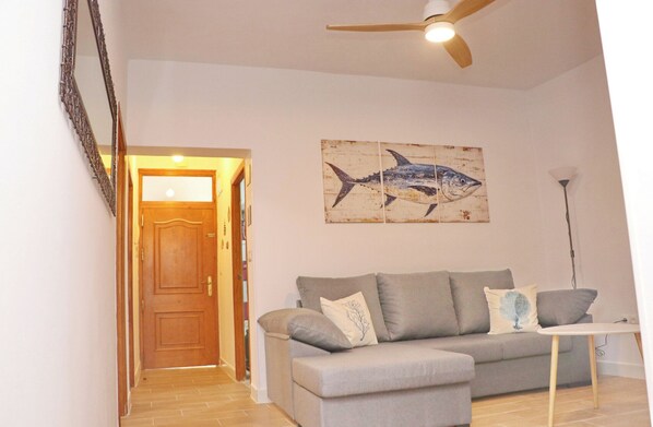 A living room with a grey sofa, a wooden door, a ceiling fan, and a fish painting on the wall.