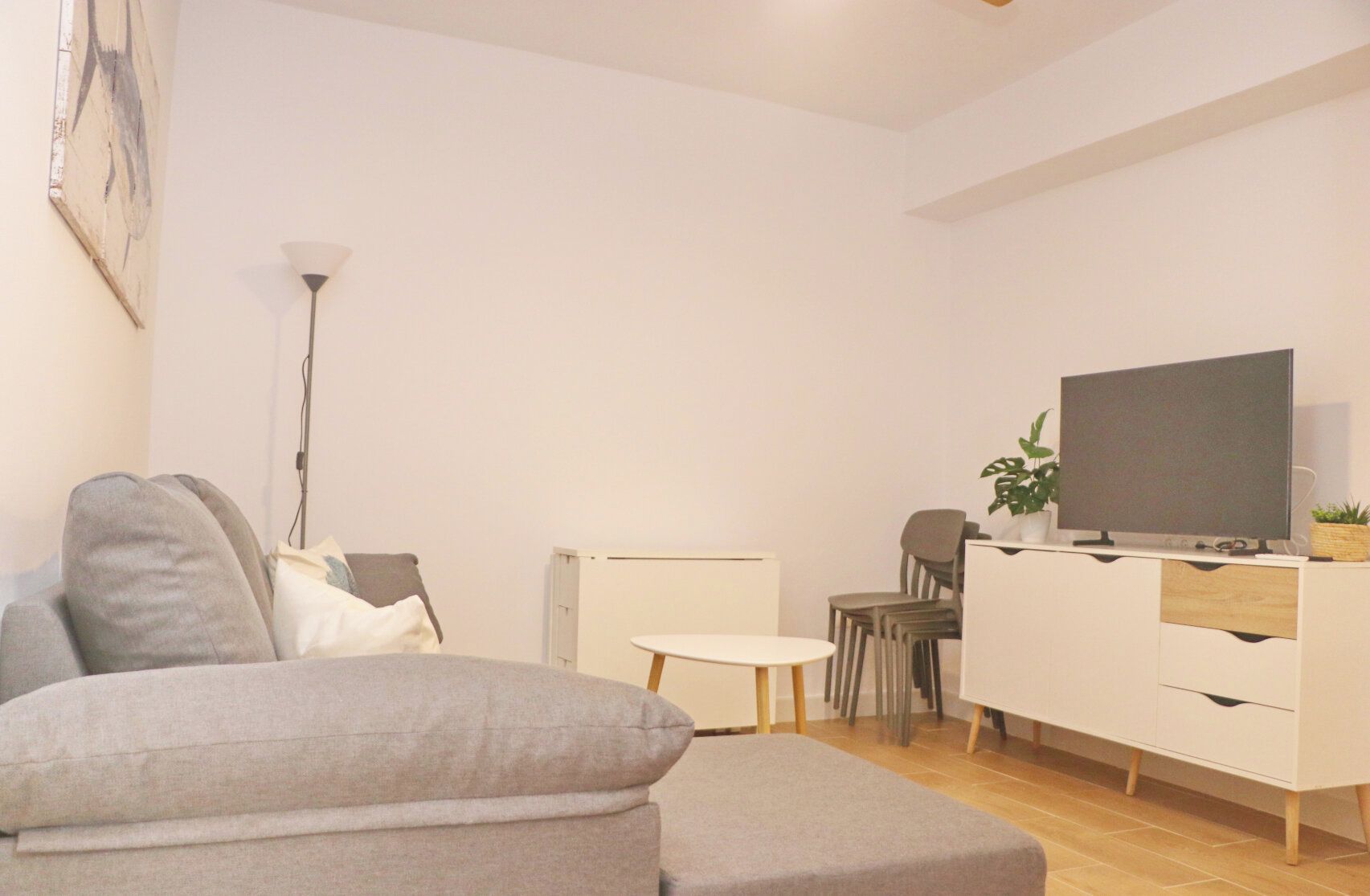 Un salon moderne avec un canapé gris, une petite table ronde, un meuble blanc et un téléviseur à écran plat.