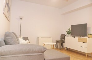 Una sala de estar moderna con un sofá gris, una mesita redonda pequeña, un armario blanco y un televisor de pantalla plana.