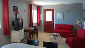 A living room with a red sofa, a television on a white cabinet, a dining table with chairs, and a door with a window. - Holiday Home with Pool, Mountain View, Wi-Fi and Air Conditioning (Callas)