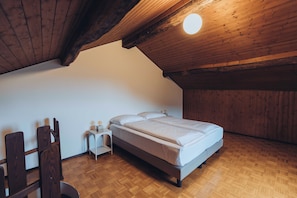 Una camera da letto con soffitto in legno, un letto, un comodino e una sedia.