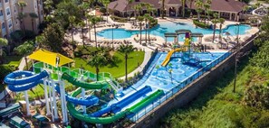 Parque acuático con toboganes y piscinas múltiples, rodeado de palmeras y un edificio de hotel.