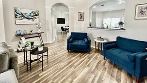 Un salon spacieux doté d’un plancher en bois, d’un fauteuil bleu, d’un canapé bleu et d’une petite table ronde agrémentée d’objets décoratifs.