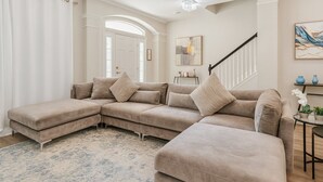 Un canapé d’angle beige, accompagné d’un pouf assorti, d’une petite table d’appoint et d’un escalier doté d’une rampe.