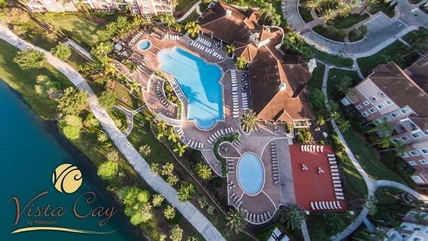 An aerial view of a resort with multiple swimming pools, a central circular pool, and a red-roofed area.