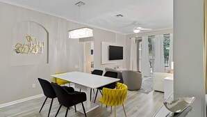 Un espace repas moderne avec une table blanche, des chaises noires et jaunes, un téléviseur à écran plat et une table basse en verre.
