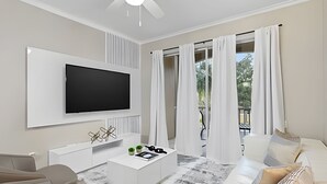 Un salon moderne avec un téléviseur à écran plat fixé au mur, un canapé blanc, une table basse agrémentée d’objets décoratifs et un balcon avec des rideaux blancs.