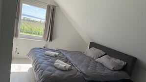 A bedroom with a bed, pillows, and a view of a green landscape through a window. - Vacation villa "Twin Garden" in Zánka, 5 minutes from Lake Balaton. Garden & Terrace. (Zánka)