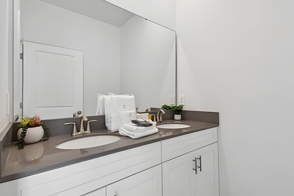 Un baño moderno con dos lavamanos, un espejo grande y muebles blancos.