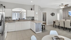 Une cuisine moderne avec des meubles blancs, un îlot central et un coin repas comprenant une table ronde et des chaises.